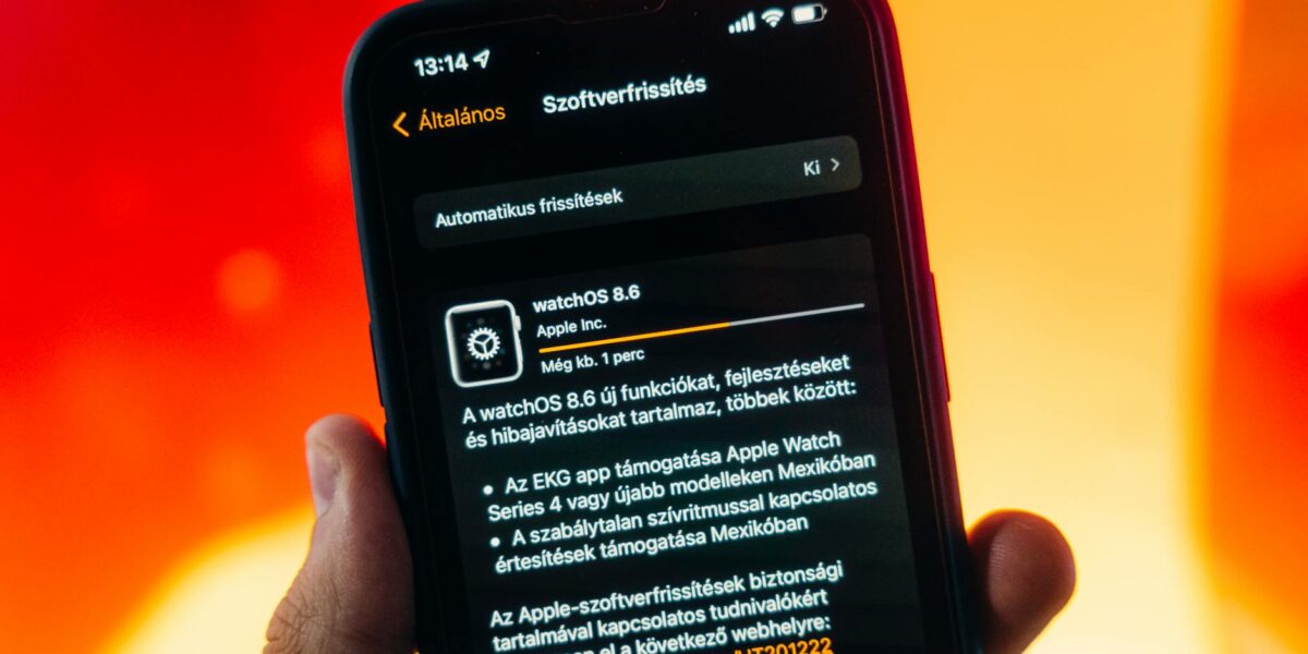 Hand holding a smartphone displaying WatchOS 8.6 update notification against warm gradient background.