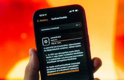 Hand holding a smartphone displaying WatchOS 8.6 update notification against warm gradient background.