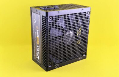 Black computer power supply unit with fan displayed against yellow background.