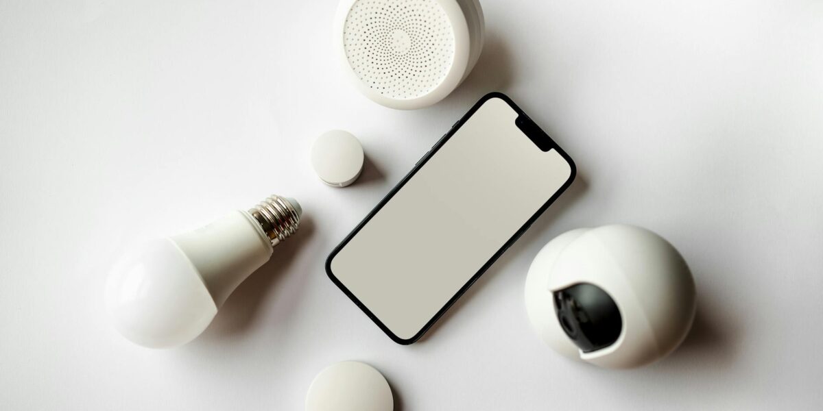 Flat lay of smartphone and smart home devices on a white backdrop, showcasing modern technology.