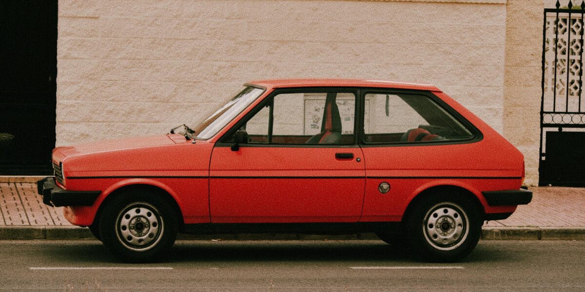 A classic red hatchback car parked beside a white stone wall in Torrevieja, Spain.
