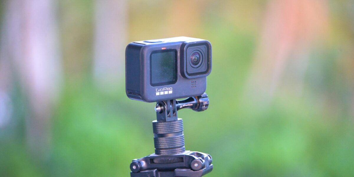 Close-up of a GoPro action camera mounted on a tripod set against a blurred outdoor background.