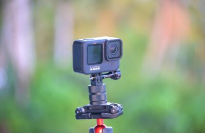 Close-up of a GoPro action camera mounted on a tripod set against a blurred outdoor background.