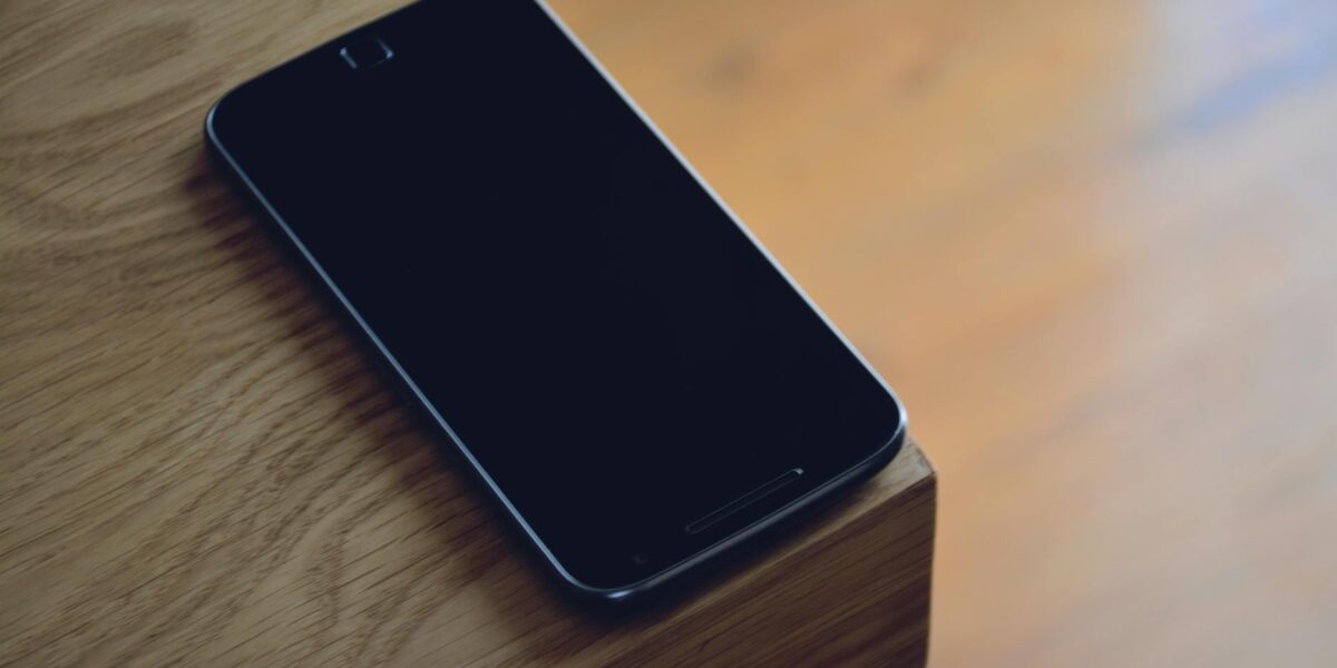 A smartphone sits quietly on the edge of a wooden table, displaying modern technology's sleek design.