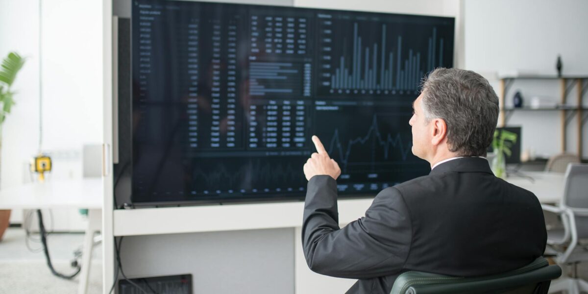 A businessman sitting and analyzing financial data on a large screen in an office.