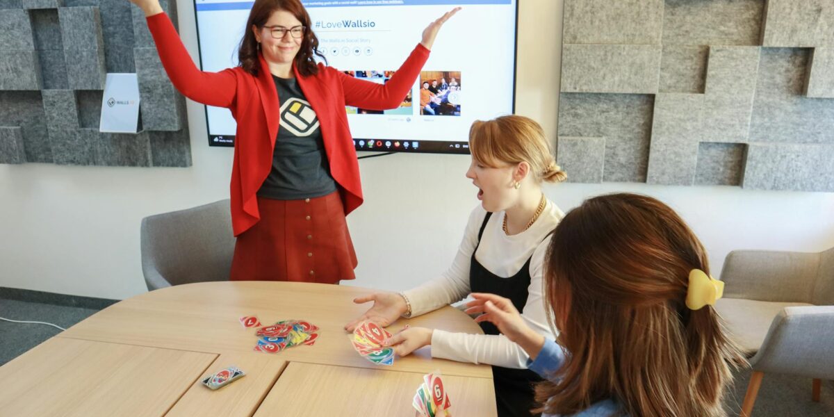 Three women engage in a lively team building card game in a modern office setting.