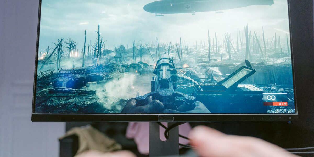 A person playing a video game on a high-resolution monitor, showcasing a war-themed landscape.
