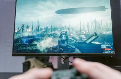 A person playing a video game on a high-resolution monitor, showcasing a war-themed landscape.