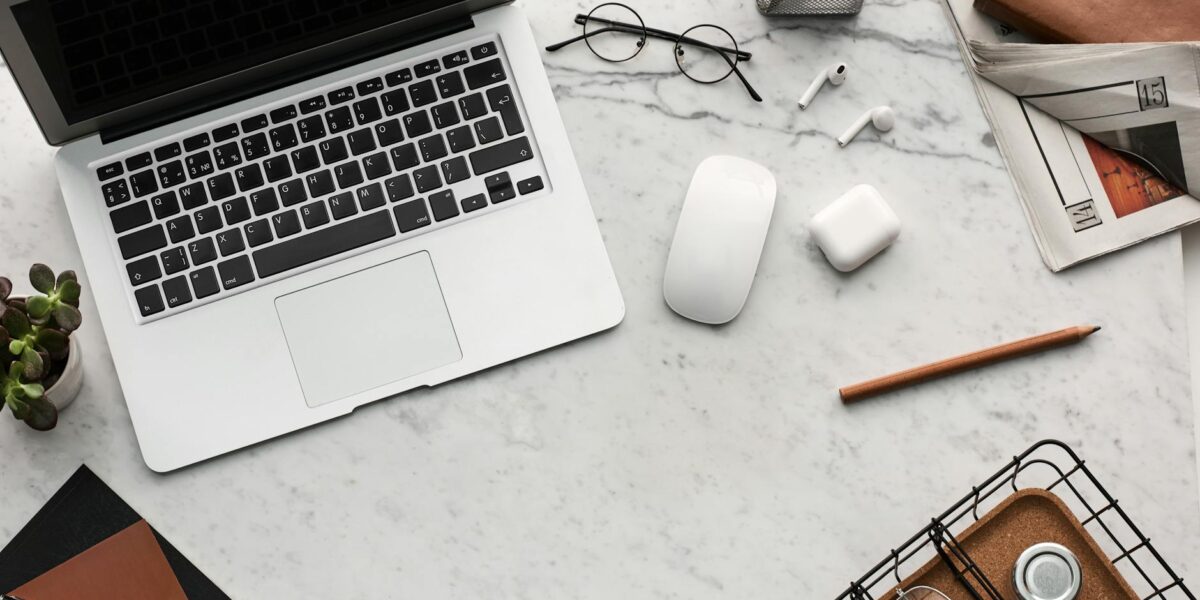 Discover a clean, organized workspace featuring a laptop, AirPods, and stationery essentials on a marble desk.