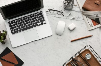 Discover a clean, organized workspace featuring a laptop, AirPods, and stationery essentials on a marble desk.