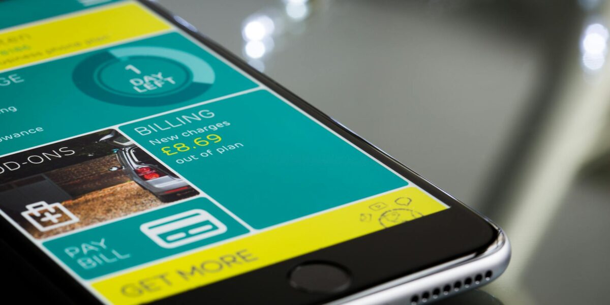 Close-up of a smartphone displaying a billing app interface on a reflective surface.