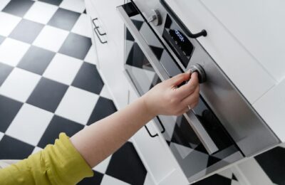Hand adjusting the temperature dial on a modern stainless steel oven in a contemporary kitchen.