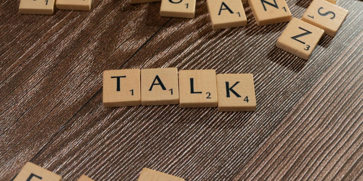 Wooden letter tiles on a table spelling 'Talk', ideal for language and communication themes.