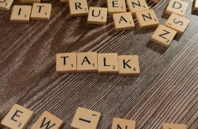 Wooden letter tiles on a table spelling 'Talk', ideal for language and communication themes.