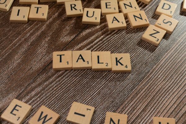 Wooden letter tiles on a table spelling 'Talk', ideal for language and communication themes.