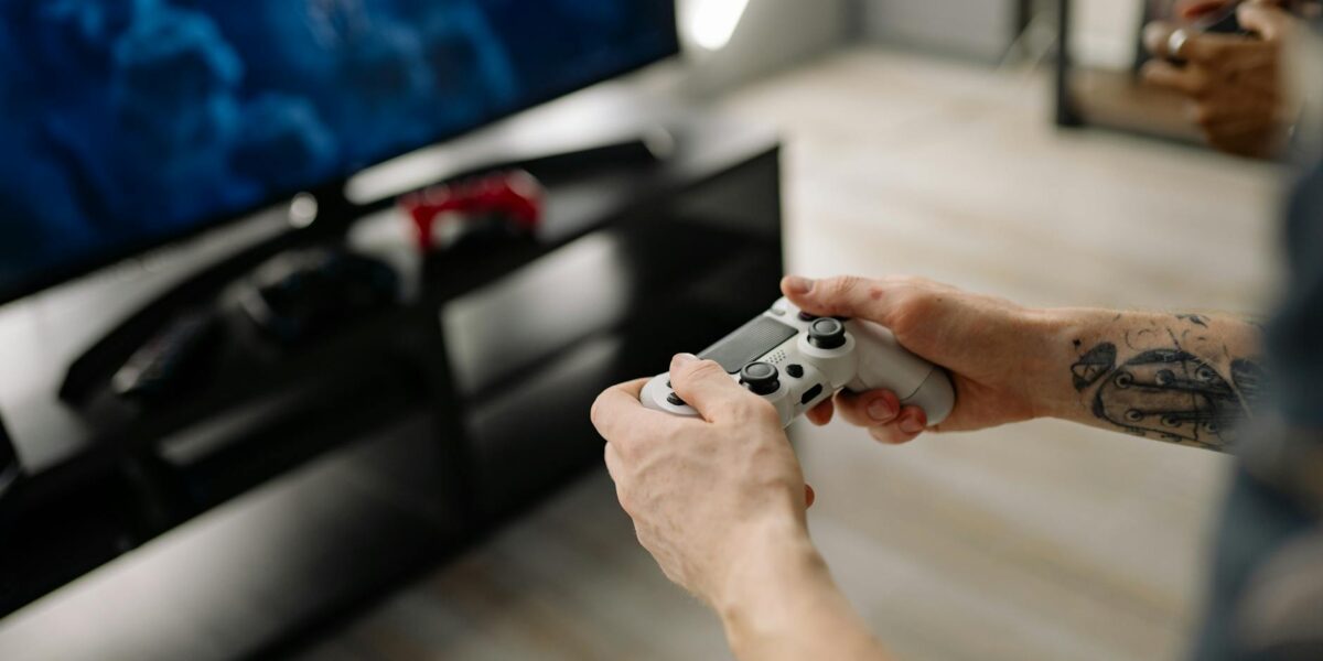 Person playing video games using a game controller indoors on a modern TV setup.
