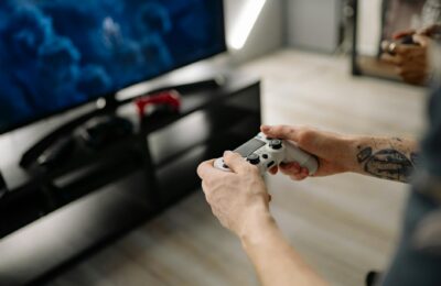 Person playing video games using a game controller indoors on a modern TV setup.