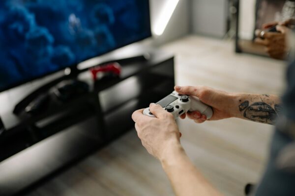 Person playing video games using a game controller indoors on a modern TV setup.
