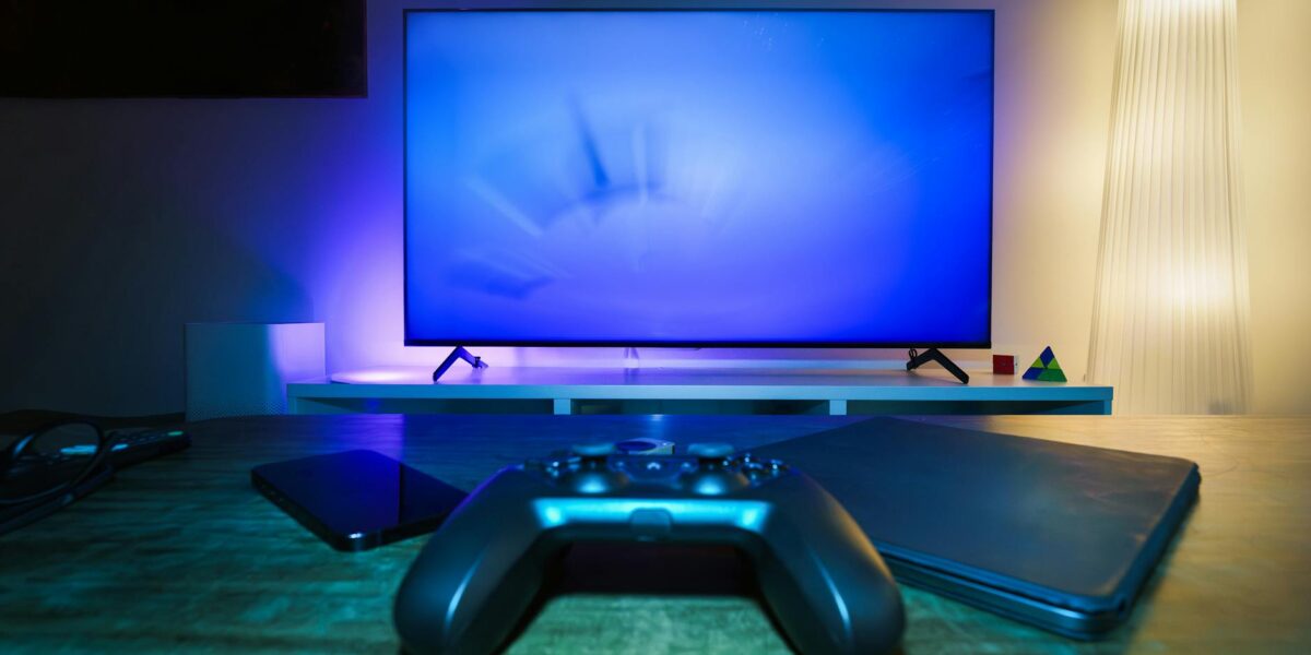 A stylish and ambient gaming setup featuring a controller, smart devices, and a TV in a lit living room.