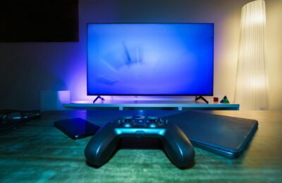 A stylish and ambient gaming setup featuring a controller, smart devices, and a TV in a lit living room.