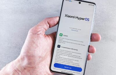 Close-up of a hand holding a Xiaomi smartphone with HyperOS interface, showcasing comprehensive refactoring and system update details.