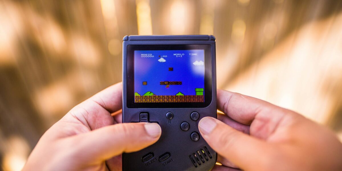 A close-up of hands holding a retro game console playing a classic Mario game outdoors.