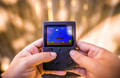 A close-up of hands holding a retro game console playing a classic Mario game outdoors.