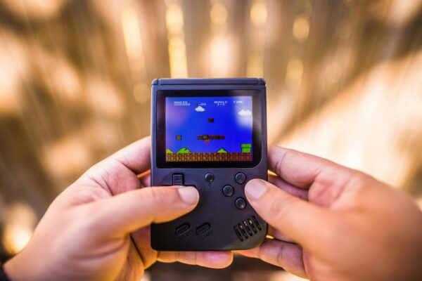A close-up of hands holding a retro game console playing a classic Mario game outdoors.