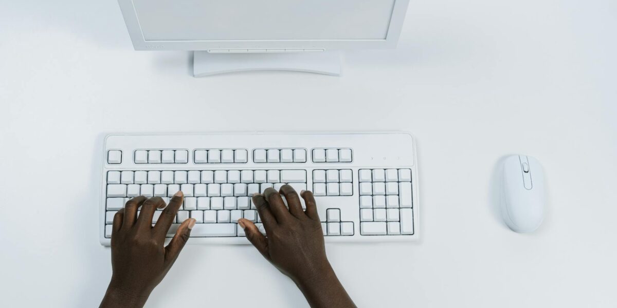 Overhead view of hands typing on white computer setup with mouse.