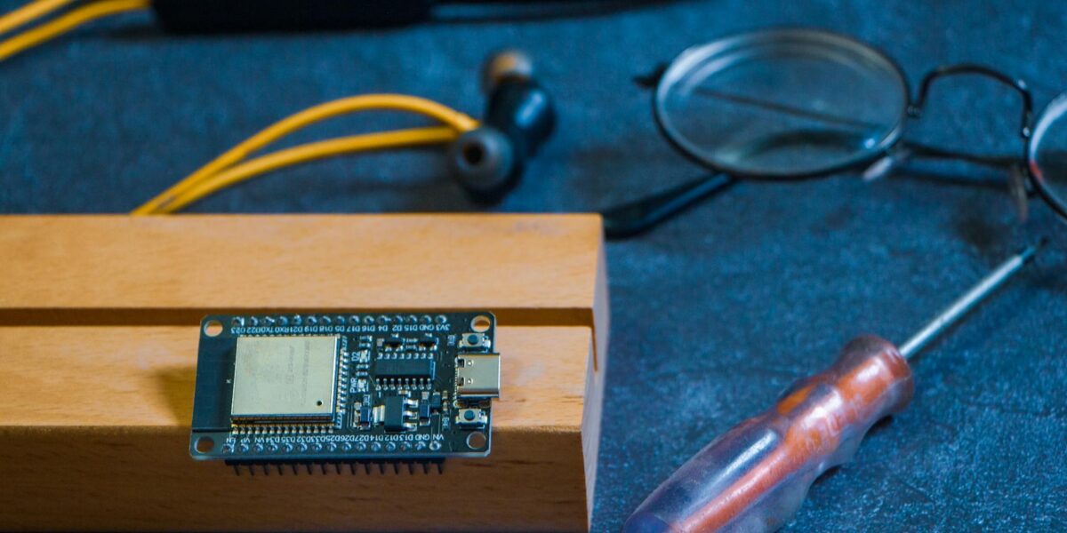Close-up of an Arduino circuit board on a workshop table with tools and gadgets, showcasing DIY electronics.