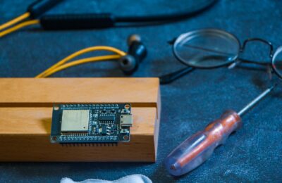 Close-up of an Arduino circuit board on a workshop table with tools and gadgets, showcasing DIY electronics.
