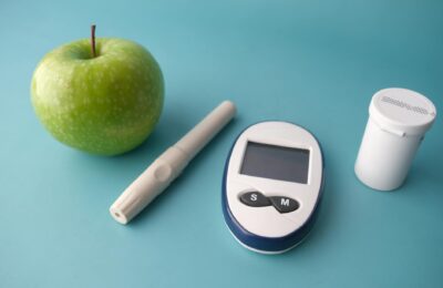 Flat lay of a glucose monitor, apple, and insulin pen on a pastel background.
