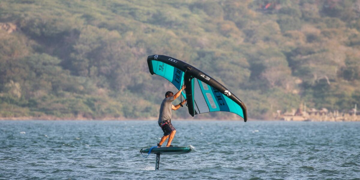 A man performing wing foiling on the ocean during summer with scenic background.