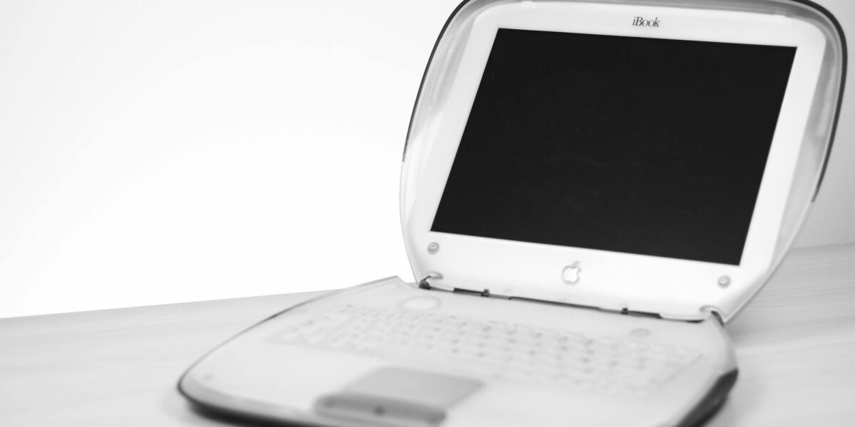 Classic iBook laptop with keyboard and screen displayed on a desk in monochrome.