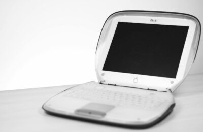 Classic iBook laptop with keyboard and screen displayed on a desk in monochrome.