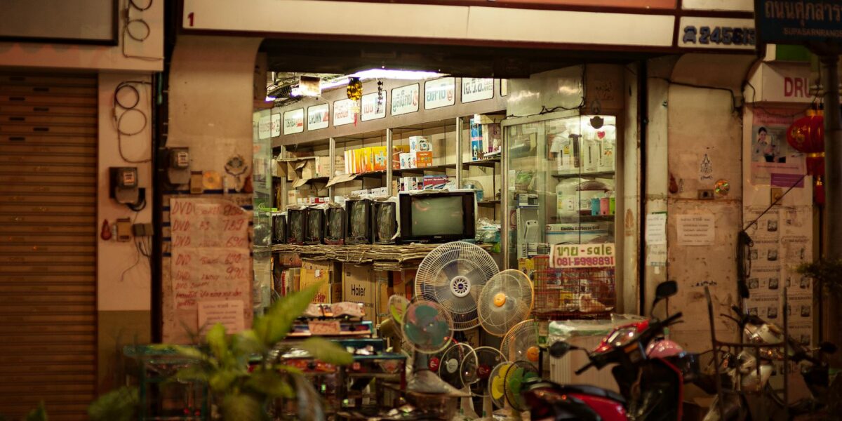 A well-lit vintage electronics store with retro TVs and fans on display, viewed from the street.