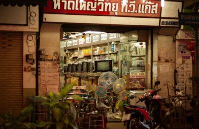 A well-lit vintage electronics store with retro TVs and fans on display, viewed from the street.