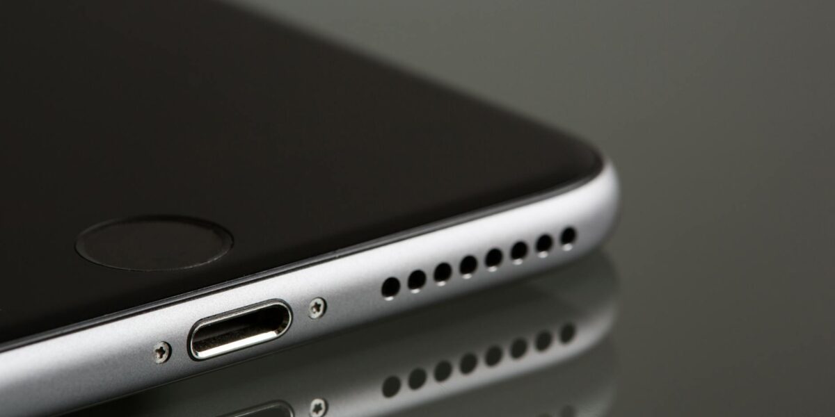 A sleek smartphone close-up highlighting its lightning connector and speaker, reflecting on a surface.
