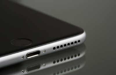 A sleek smartphone close-up highlighting its lightning connector and speaker, reflecting on a surface.