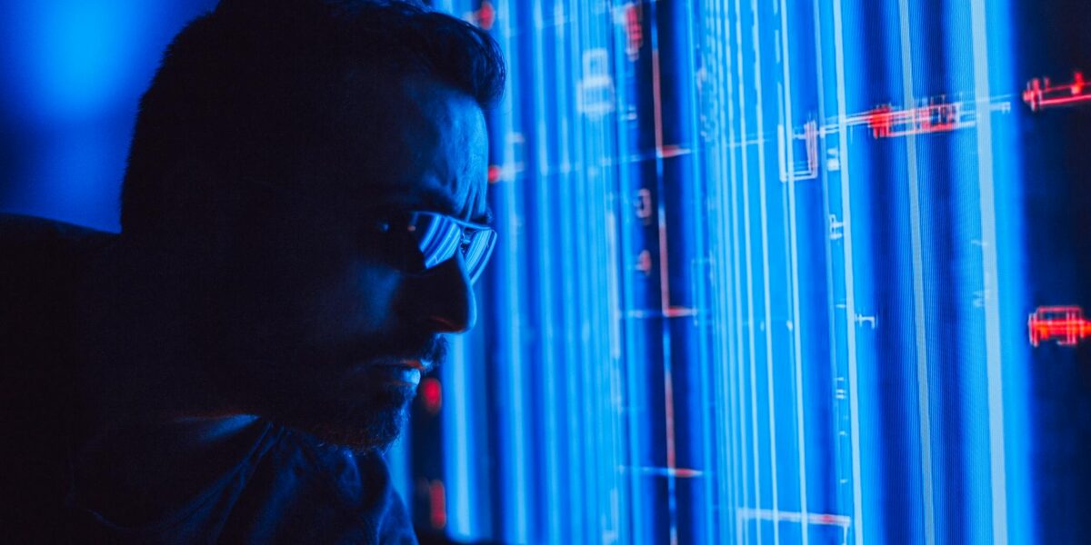 A man in sunglasses intently studies a vibrant blue holographic screen, symbolizing digital technology.