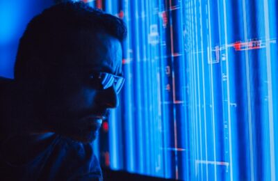 A man in sunglasses intently studies a vibrant blue holographic screen, symbolizing digital technology.