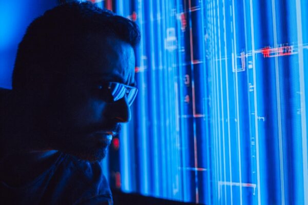 A man in sunglasses intently studies a vibrant blue holographic screen, symbolizing digital technology.