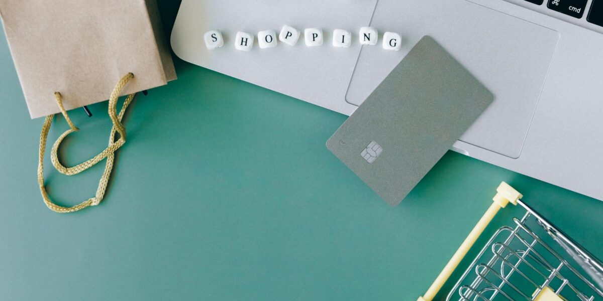 Flat lay of online shopping essentials with laptop, card, and shopping cart.