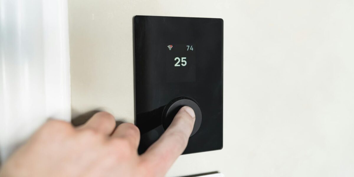 Close-up of a hand adjusting a sleek, modern smart thermostat on a wall.