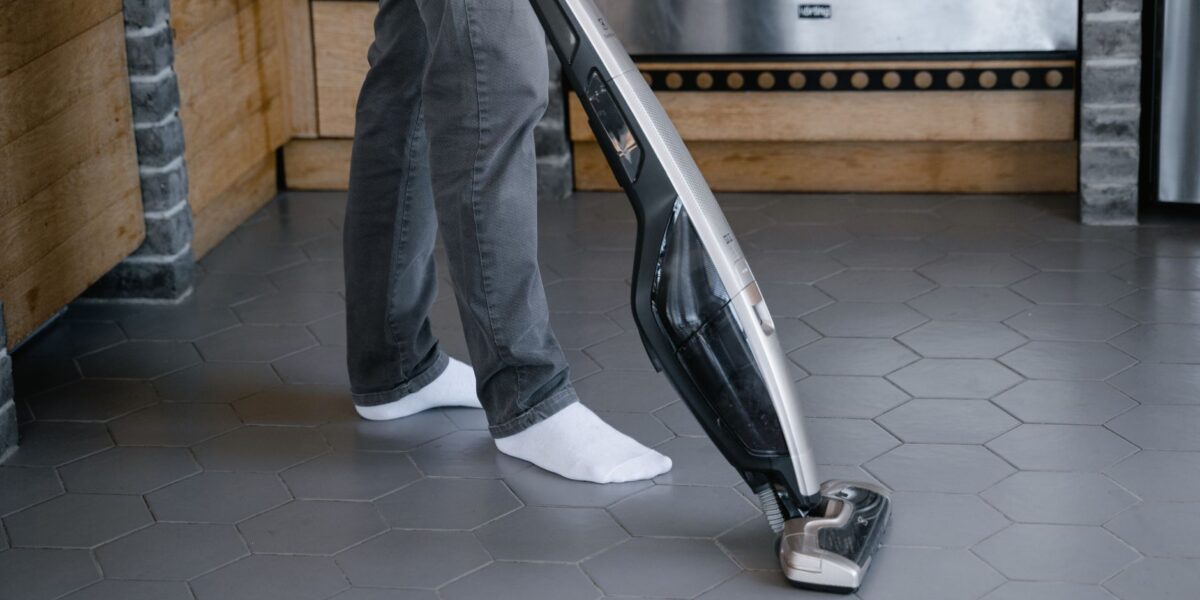 A person cleaning a tiled floor with a modern vacuum cleaner indoors.