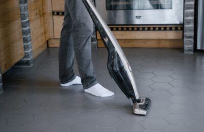 A person cleaning a tiled floor with a modern vacuum cleaner indoors.