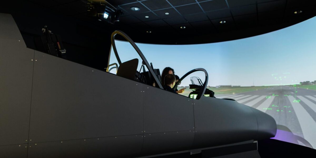 A female pilot operates a flight simulator in an advanced training facility.