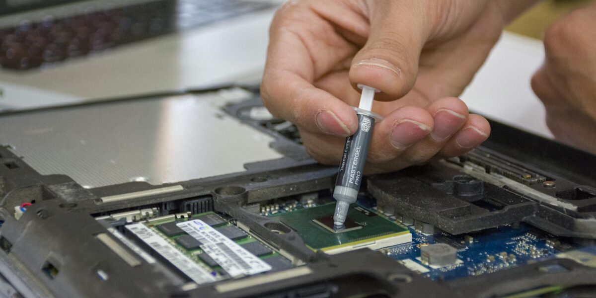 Close-up of hand applying thermal paste to a laptop microchip for maintenance.