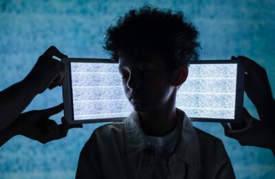 A teenager stands with eyes closed between two tablets showing digital noise, symbolizing information overload.