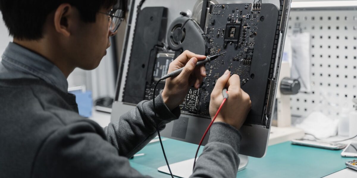 A technician works on a computer motherboard using tools at a workspace, focusing on electronics repair.